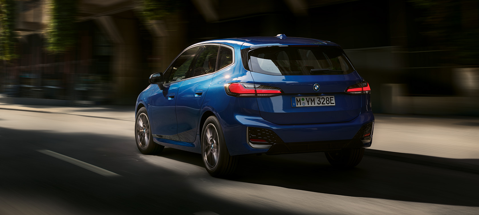 BMW 2 Serisi Active Tourer 230e plug-in hybrid U06, Metalik M Mavi/Portimao, şehir içinde sürüş sırasında arka çaprazdan görünüm