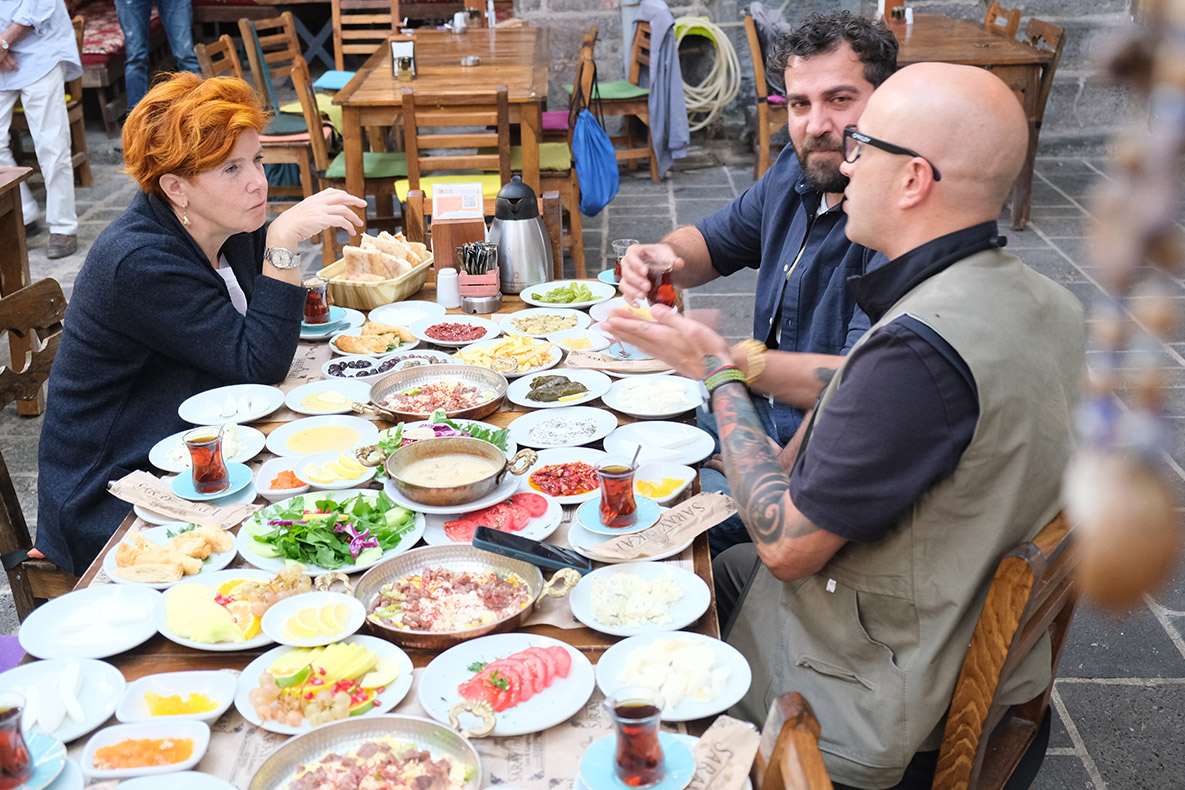 Diyarbakır’ı ziyaret edeceğimiz günü sabırsızlıkla bekliyordum ve sonunda buradayız. Zamanımız oldukça kısıtlı olmasına rağmen olabildiğince etkili kullanmaya çalışacağız. İlk durağımız Palace Gate Cafe & Breakfast’ta Şemsa ve Maksut ile buluşuyoruz. Diyarbakır’ın serpme kahvaltısını henüz denemediyseniz, ilk denemenizi burada yapabilirsiniz. Palace Gate Cafe & Breakfast ayrıldıktan sonra kendimizi Ciğerci Ramazan’da buluyoruz. Kahvaltıda doyasıya yememişiz gibi burada ara sıcaklara adeta saldırıyor, üstüne bir de kebapları mideye indiriyoruz. Buranın kebapları, bu lezzet yolculuğunda yediğim kebaplar arasında ilk beşe girer. Sonrasında ağzımız tatlansın diyerek Kadayıfçı Sıtkı Usta’nın Sur’daki şubesinin yolunu tutuyoruz. Buranın kadayıfları, hele hele fıstıklı kadayıkları yeme de yanında yat tadında. Diyarbakır ile Mardin arasında yer alan tarihî yapı ve askerî yerleşim alanı Zerzevan Kalesi’ne ziyaretimizin ardından Fırın-ci Sur’a geçiyoruz. Aslında pek aç değiliz, bize bir kâse çorba yeter de artar. Fakat masamıza ikramlar geldikçe geliyor, biz de geldikçe yiyoruz. Günü bitirirken, BMWlicious projesi kapsamında çıktığımız lezzet yolculuğunun son durağı burası oluyor. Bu proje sayesinde ülkemizin geleneksel, kültürel ve folklorik değerlerini, zenginliklerini ve en önemlisi lezzetlerini bir kez daha keşfedebildiğim için kendimi çok şanslı hissediyorum. Şemsa, Maksut ve benim rotalarımız ve dolayısıyla keşiflerimiz birbirinden oldukça farklıydı. E, zaten bu farklılık da ülkemizin en güzel yanlarından biri değil mi? Bu projenin gerçekleşmesini sağlayan BMW ailesine ve tüm ekiplere katkı ve desteklerinden dolayı teşekkürlerimi yolluyorum. Başka bir lezzet yolculuğunda görüşmek üzere.