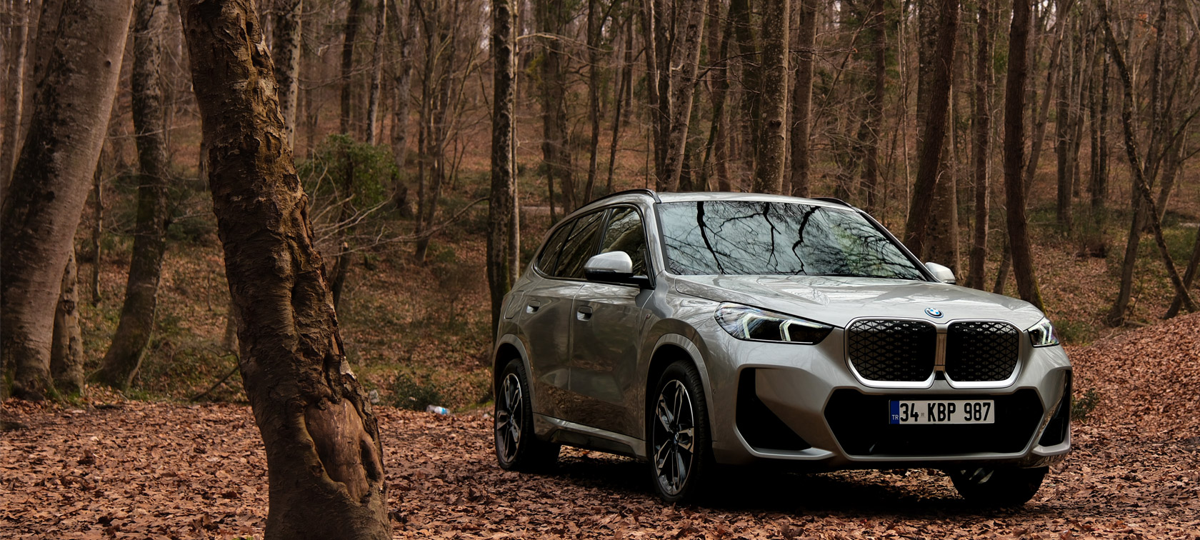 BMW iX1 U11 BEV, Metalik Beyaz/Mineral, Virajlı dağ yolunda sürüş sırasında ön çaprazdan görünüm